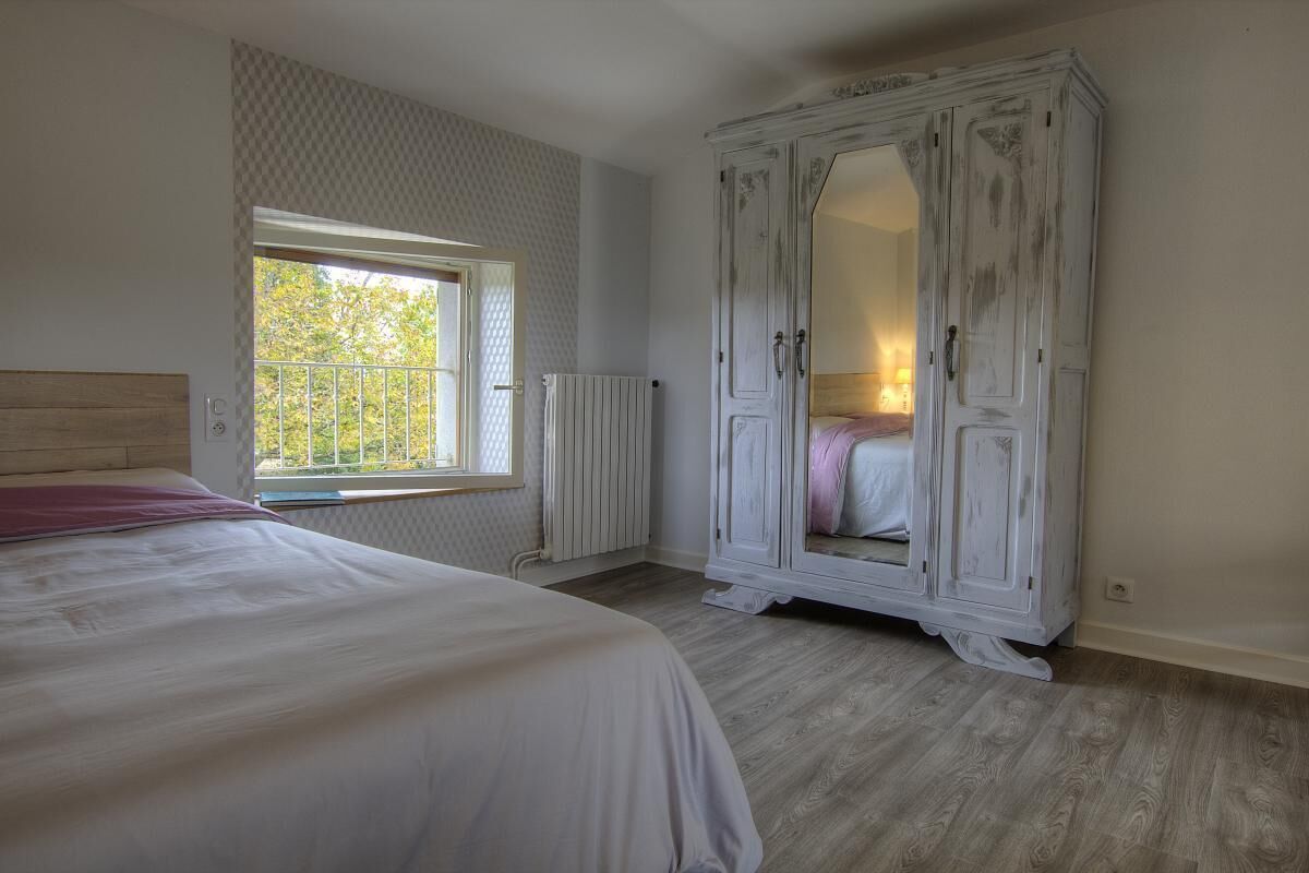Une chambre avec un grand lit, une armoire, un radiateur et une fenêtre donnant sur des arbres.