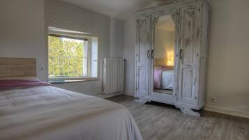 Une chambre avec un grand lit, une armoire, un radiateur et une fenêtre donnant sur des arbres.