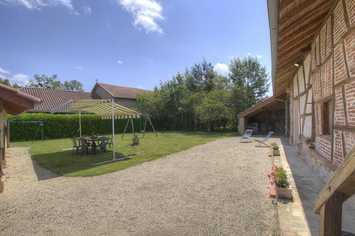 Ein Innenhof mit Kiesweg, überdachter Sitzgelegenheit und einem Backsteinhaus mit geneigtem Dach.