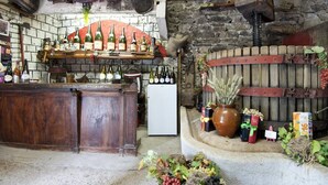 A rustic bar area with wooden shelves holding bottles, a refrigerator, and a stone wall backdrop.