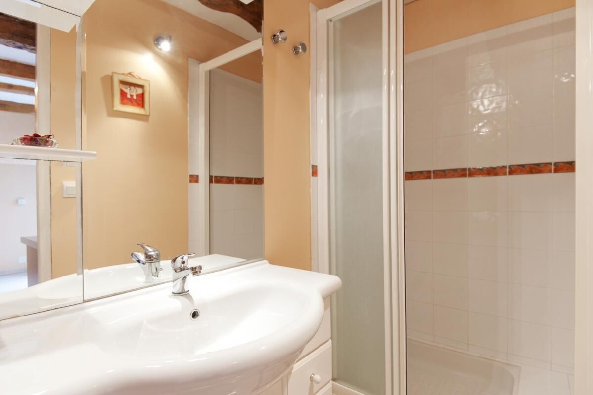 A bathroom with a large mirror, a sink, and a shower area.
