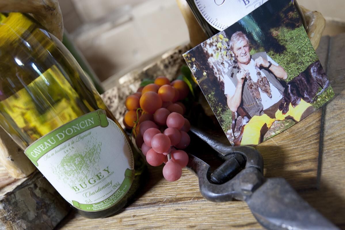 Una botella de vino Cuvée d'Oncin, un par de tijeras de podar y un racimo de uvas rojas sobre una superficie de madera.
