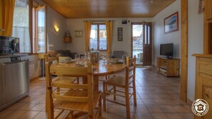 A spacious kitchen with wooden cabinets, a dining table with chairs, a built-in oven, and a television in the corner. - Futin - Outriaz - Gîte (OUTRIAZ)