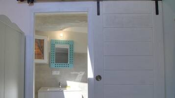 A bathroom with a white door, a mirror, and a sink.