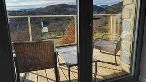 A balcony with wicker chairs and a table, overlooking a scenic landscape with hills and trees. - Beaume d’ataraxie - Beautiful View Room (Apt. 4) (Solignac-sur-Loire)
