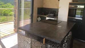 A modern kitchen with a large island, built-in oven, and a sliding glass door leading to a balcony with a scenic view. - Beaume d’ataraxie - Beautiful View Room (Apt. 4) (Solignac-sur-Loire)
