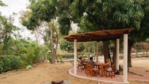 Ein Sitzbereich im Freien mit einer Pergola, Tischen und Stühlen, umgeben von Bäumen und Pflanzen.