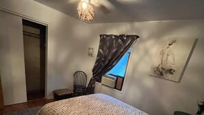 A bedroom with a bed, a chair, a window with curtains, a ceiling fan, and a wall-mounted air conditioner. - 418 W. Main, Apartment #4.

 (Luverne)
