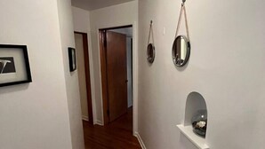 A hallway with white walls, wooden flooring, and a door at the end. There are framed pictures on the wall and a small shelf with an object on it. - 418 W. Main, Apartment #4.

 (Luverne)