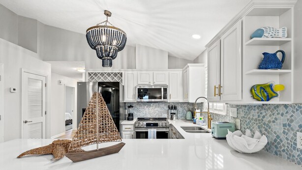 A modern kitchen with white cabinetry, a large island, a chandelier, and decorative fish on shelves. - Sunshine House! 3BR 2BA Sleeps 9! Your Perfect Retreat for Comfort and Style (Panama City Beach)