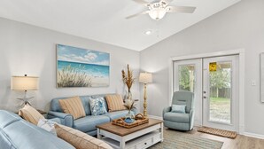 A living room with a blue sofa, a wooden coffee table, and a ceiling fan. - Sunshine House! 3BR 2BA Sleeps 9! Your Perfect Retreat for Comfort and Style (Panama City Beach)