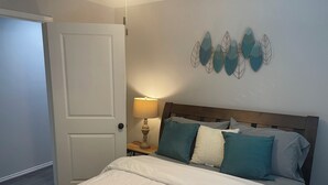 A bedroom with a bed, a nightstand with a lamp, and a wall with decorative leaf art. - Cozy two bedroom home minutes from downtown (Houston)