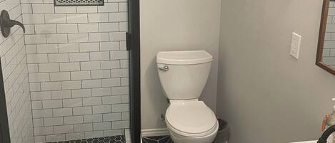 A bathroom with a shower, toilet, sink, and a tiled floor with a geometric pattern.
