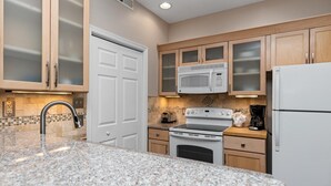 Una cucina con piani di lavoro in granito, cappa aspirante in acciaio inox, forno a microonde integrato, fornello e frigorifero.