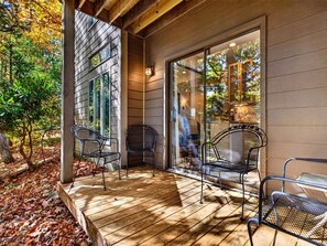 A wooden deck with metal chairs and a glass door leading to a covered area.