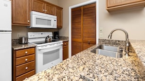 A kitchen with wooden cabinets, a white microwave, a stove, a sink, and a granite countertop. - Three Ridges 84 with Wintergreen Advantage (Wintergreen)