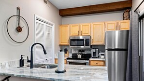A kitchen with wooden cabinets, stainless steel appliances, a marble countertop, and a wall clock. - Laurelwood 44 with Wintergreen Advantage (Wintergreen)