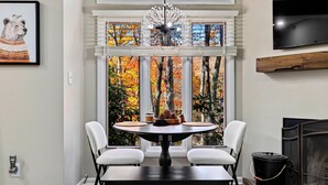 A dining area with a round table, two chairs, a chandelier, a fireplace, and a large window with autumn foliage view. - Laurelwood 44 with Wintergreen Advantage (Wintergreen)
