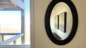 Ein gerahmtes Kunstwerk an einer Wand, ein Fenster mit Blick auf eine Holzhütte und ein Balkongeländer.