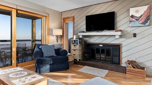Een woonkamer met een bank, een flatscreen televisie, een open haard en uitzicht door een schuifdeur.