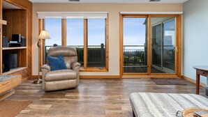 A spacious room with a leather armchair, a sofa, and a large sliding glass door leading to a balcony.