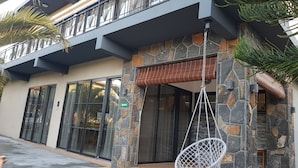 A building with a stone facade, large glass doors, and a hanging chair outside. - Villas Rocher (Fond du Sac)