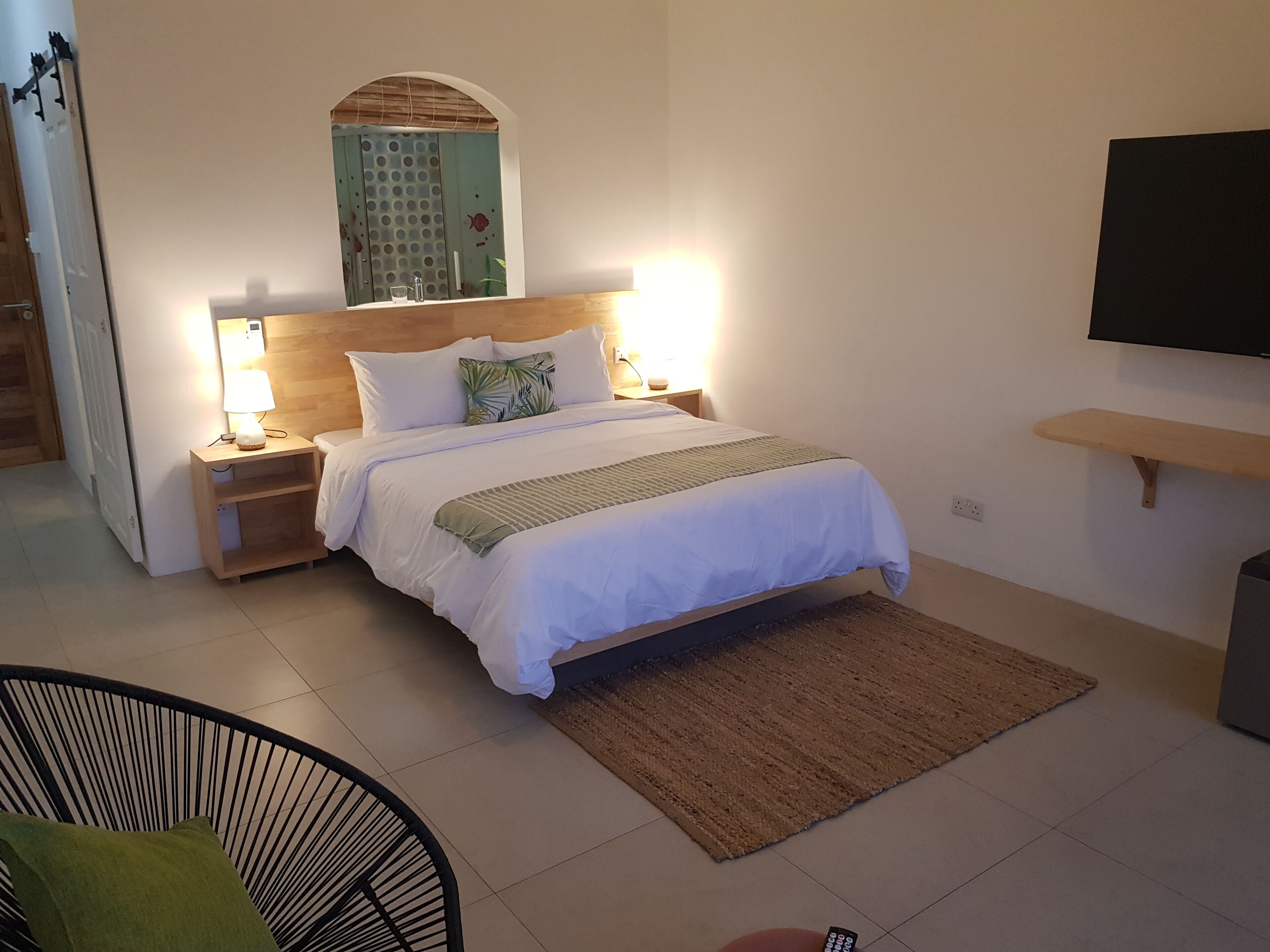 A neatly arranged bedroom with a bed, bedside lamps, a TV mounted on the wall, and a small wooden shelf.