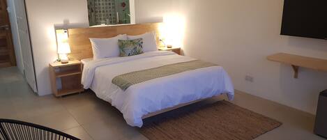 A neatly arranged bedroom with a bed, bedside lamps, a TV mounted on the wall, and a small wooden shelf.