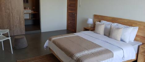 Un dormitorio con una cama grande, cabecera de madera, mesita de noche con lámpara, una silla y un armario.