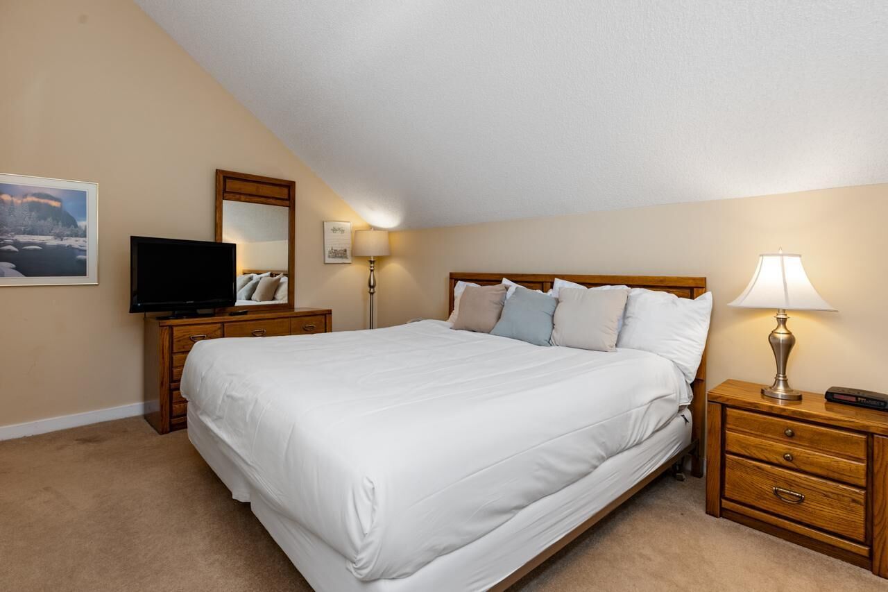 A hotel room with a large bed, a flat-screen TV, a wooden nightstand, a lamp, and a painting on the wall.