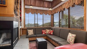 Una sala de estar moderna con un sofá seccional, una chimenea y ventanas grandes con persianas.