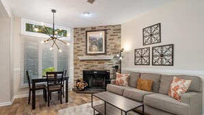 A living room with a fireplace, a dining area with a table and chairs, and a sofa with decorative pillows.