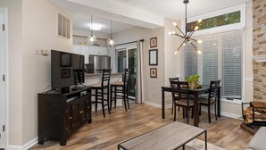 A modern kitchen with a dining area, wooden flooring, and a large window with blinds.