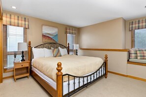 A bedroom with a large bed, a nightstand, a lamp, and a window with blinds.