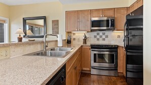 A modern kitchen with granite countertops, stainless steel appliances, wooden cabinets, and a tiled backsplash. - Overlook 43 with Wintergreen Advantage (Wintergreen)