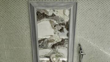 Un baño con zona de ducha, pared con azulejos y un panel tipo mármol en la puerta.