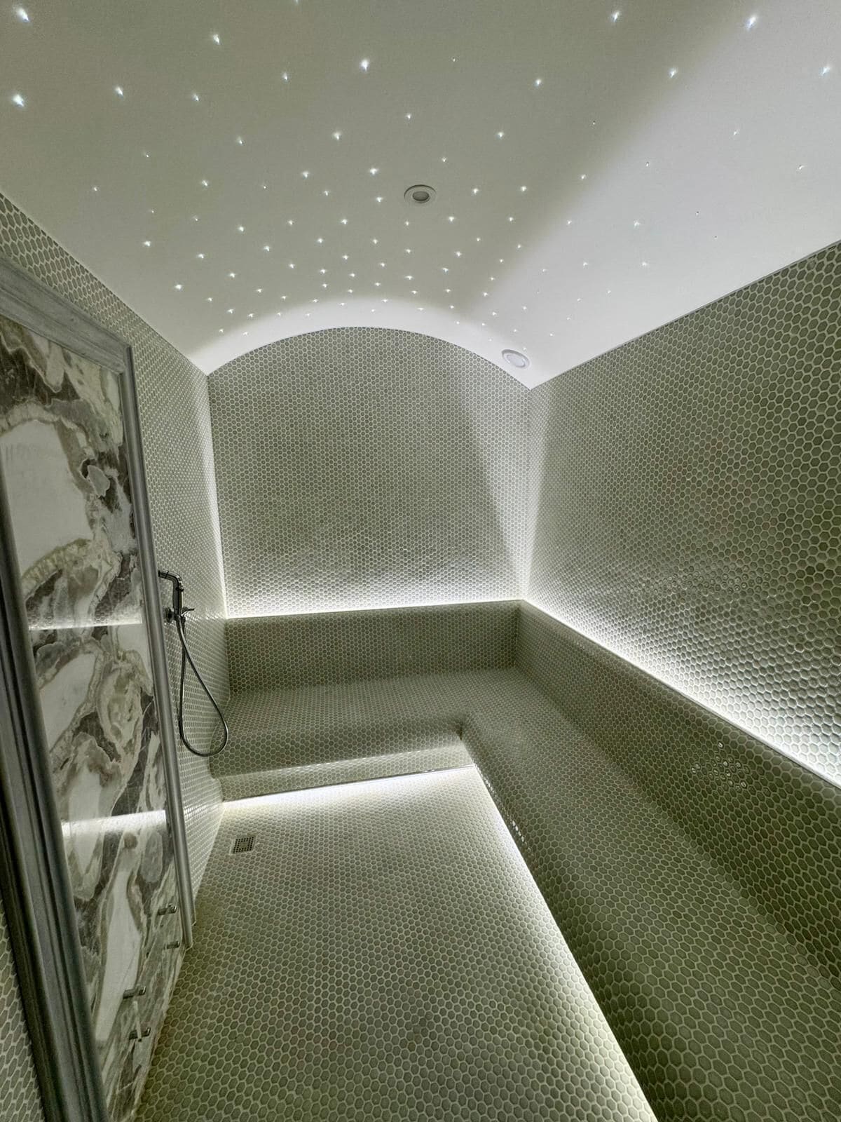 A modern bathroom with a hexagonal tile pattern, a glass shower enclosure, and recessed ceiling lights.