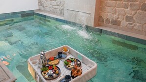 A hot tub with a tray of food and drinks, surrounded by stone walls and a skylight. - Boreas Hotel & SPA, Trademark Collection by Wyndham (Ankara)