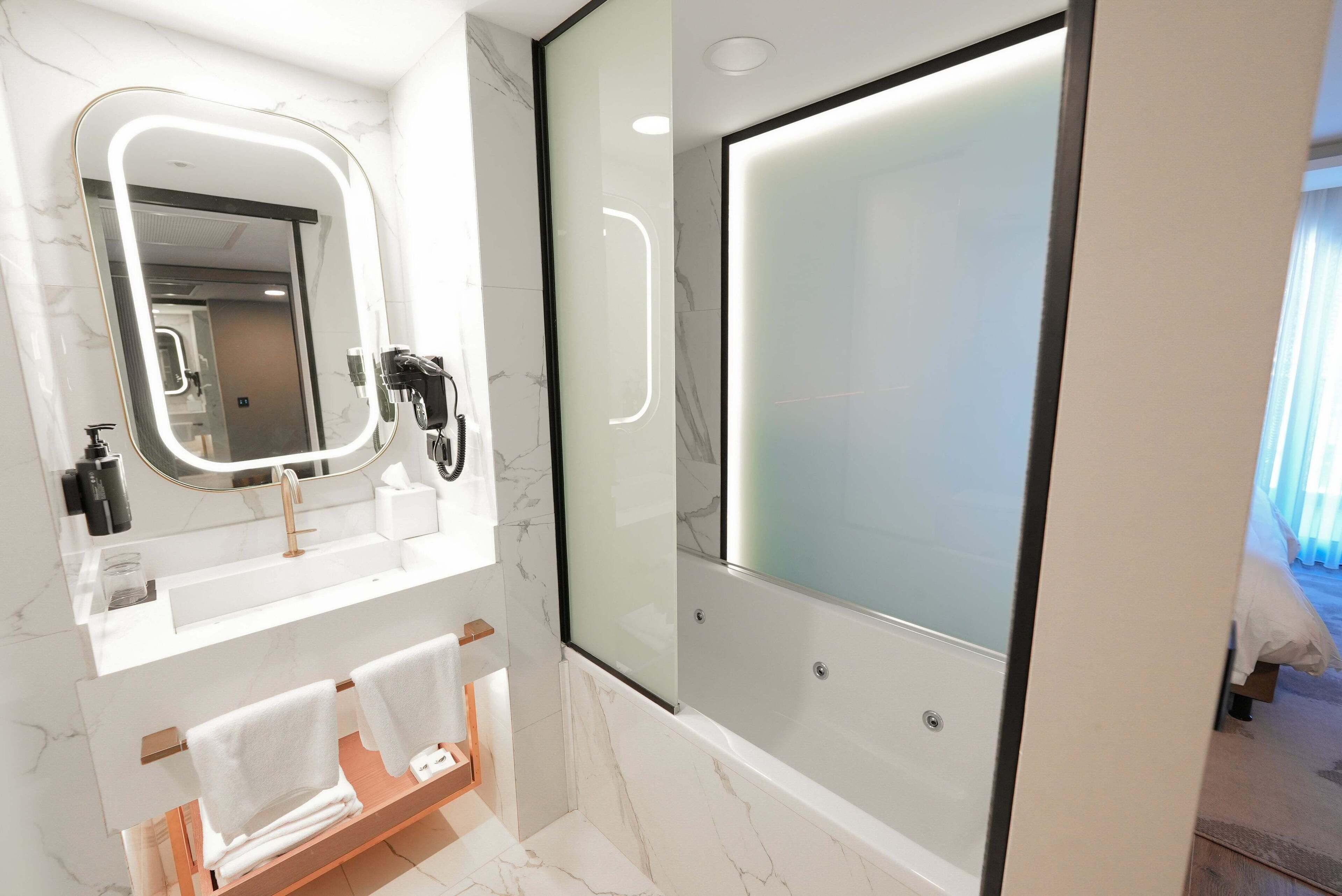 A modern bathroom with a large mirror, a bathtub, and a vanity with a towel rack.