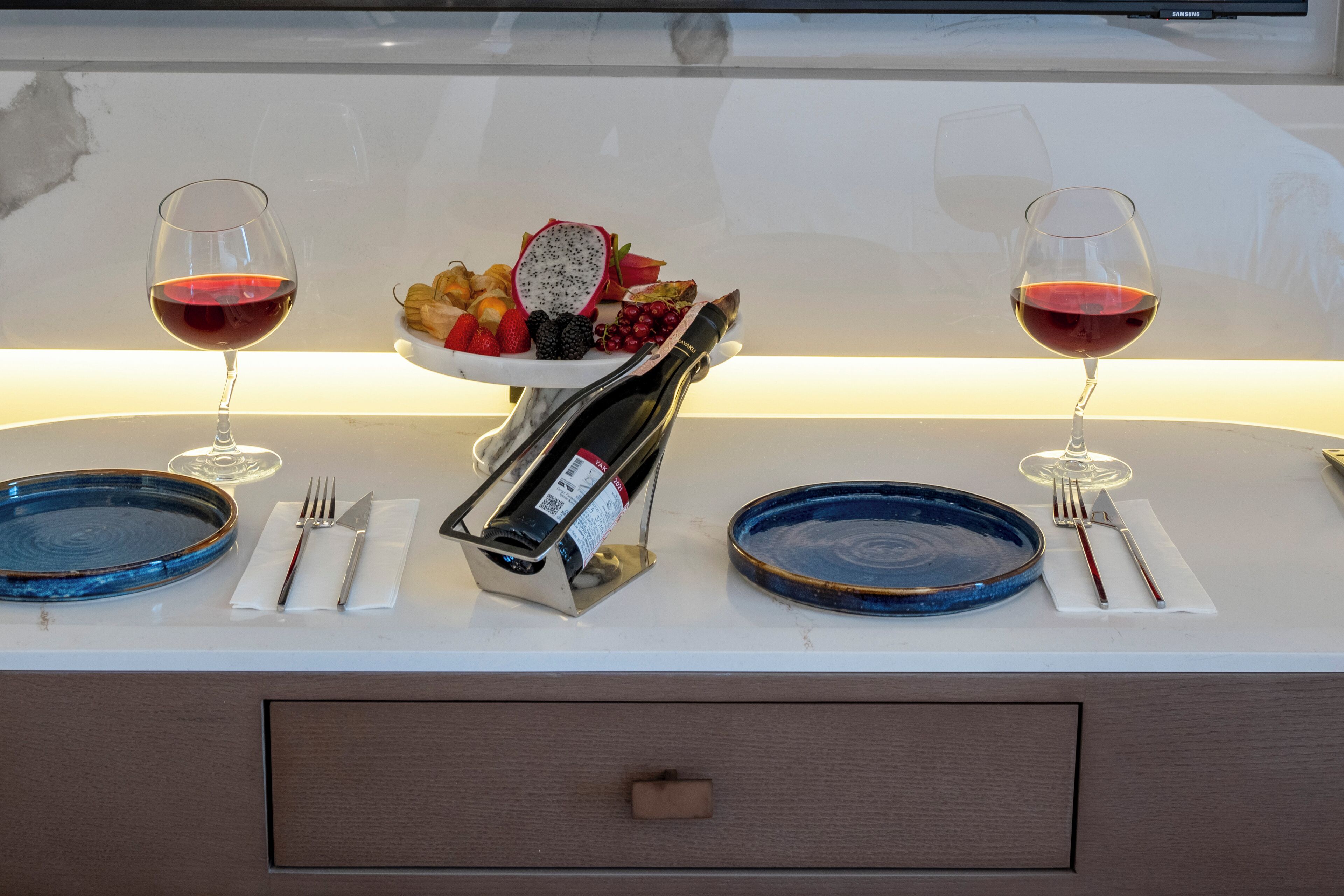 Een gedekte tafel met twee wijnglazen, een wijnfles en een schaal met fruit.