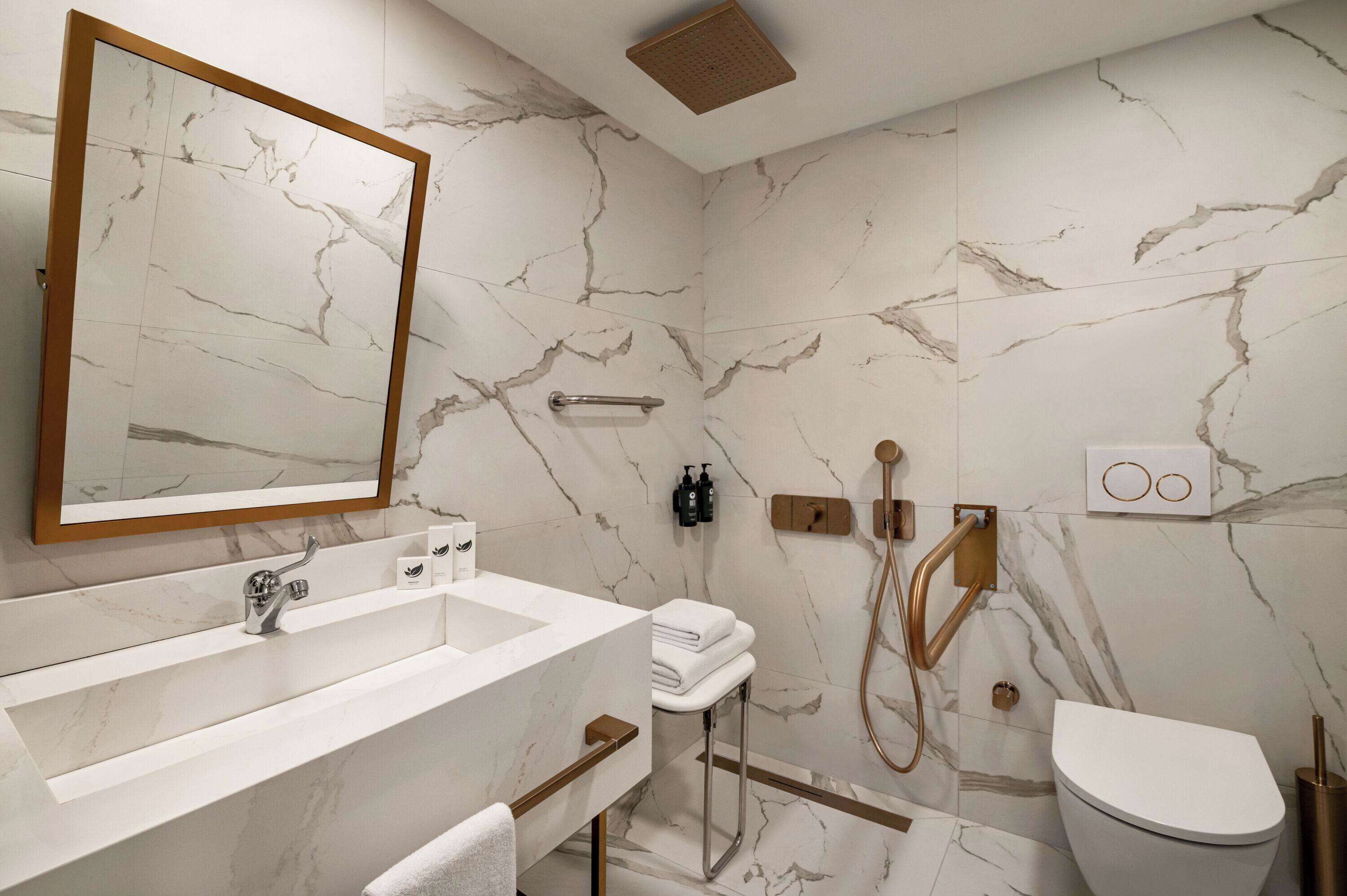 A modern bathroom with a marble backsplash, a large mirror, a sink, a toilet, and a shower area.