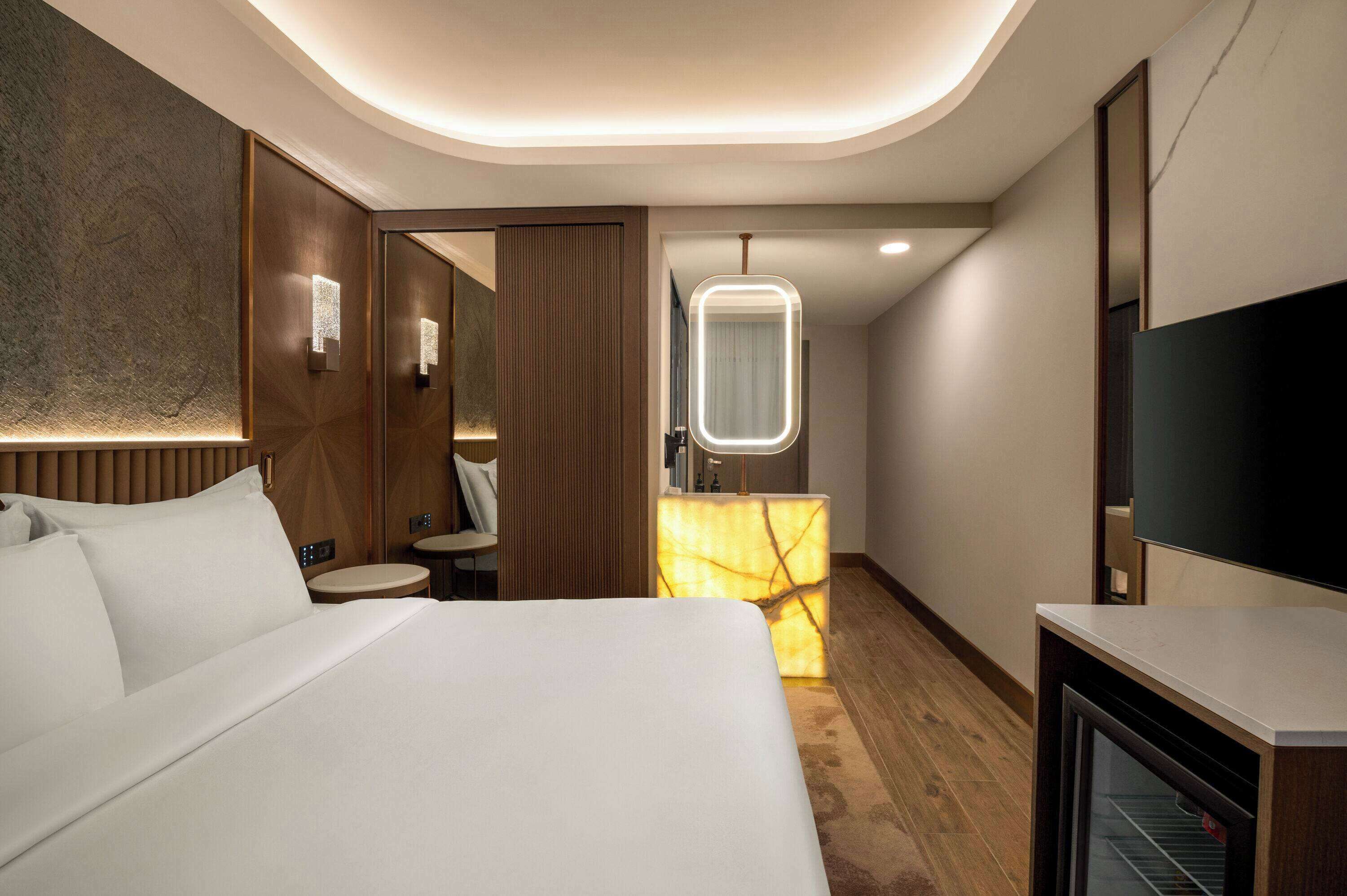 A hotel room with a large bed, a bedside table, a mirror, a small round table, and a television.