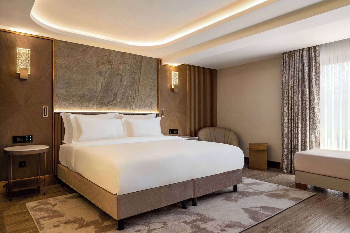 Ein modernes Hotelzimmer mit einem großen Bett, einer Sitzecke und Blick auf die Stadt.