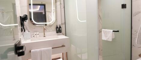 Un baño moderno con cabina de ducha de vidrio, lavamanos de mármol blanco y un espejo grande con iluminación integrada.