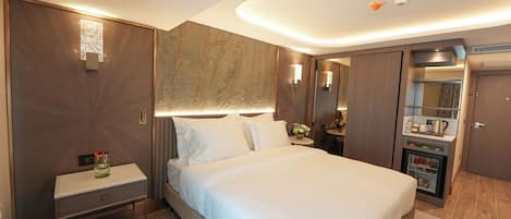 Una habitación de hotel moderna con una cama grande, una mesita de noche, un armario empotrado y un minibar.