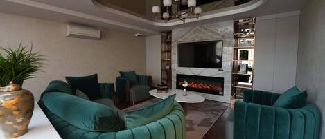 Una sala de estar moderna con sofás azul verdoso, un televisor de pantalla plana, una chimenea y una lámpara en el techo.