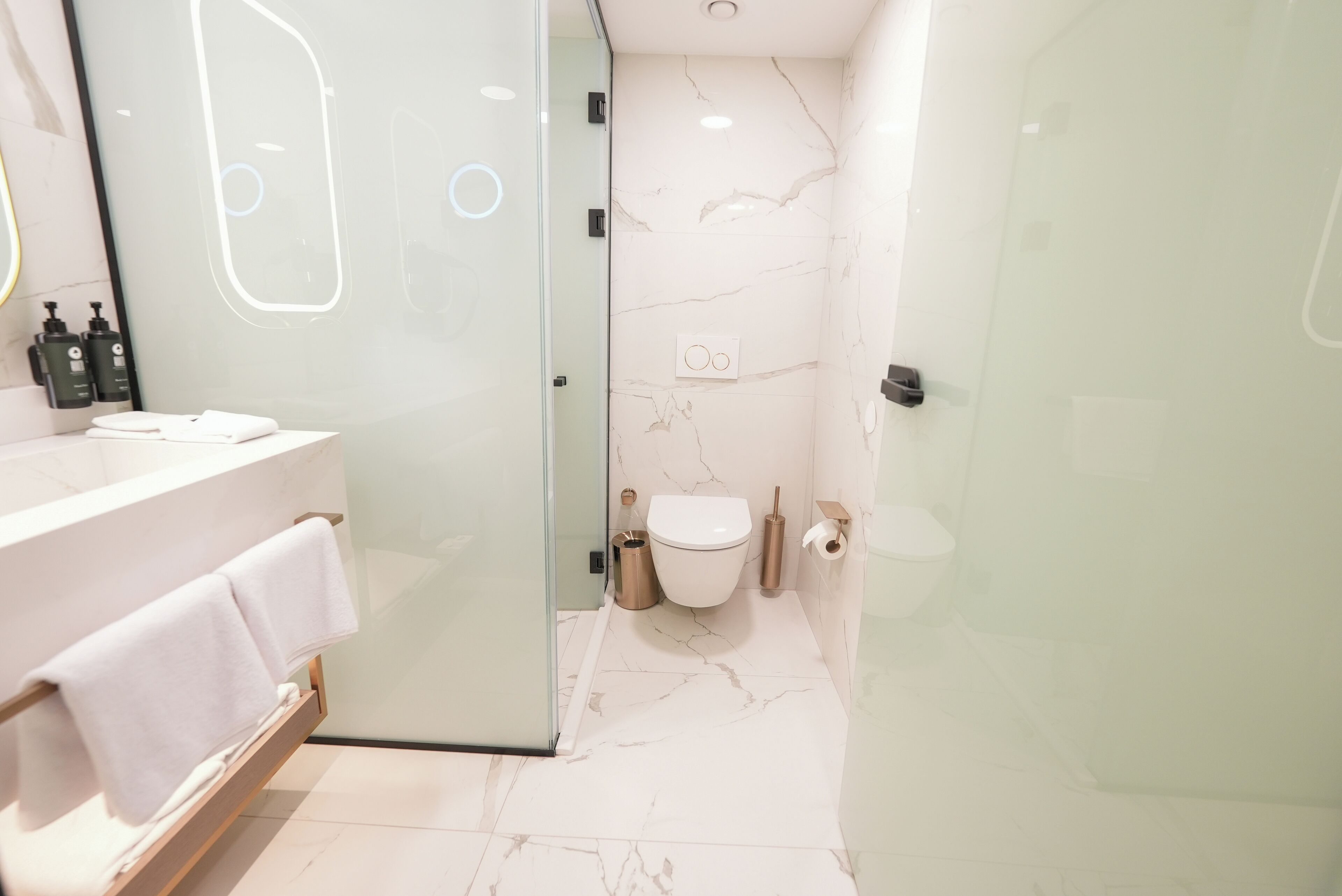Een moderne badkamer met een glazen douchecabine, een marmeren vloer, een wit toilet en een wastafelmeubel met een handdoekhouder.