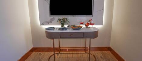 A modern living room with a flat-screen TV mounted on a marble wall, a dining table with plates, cutlery, and a vase of flowers.