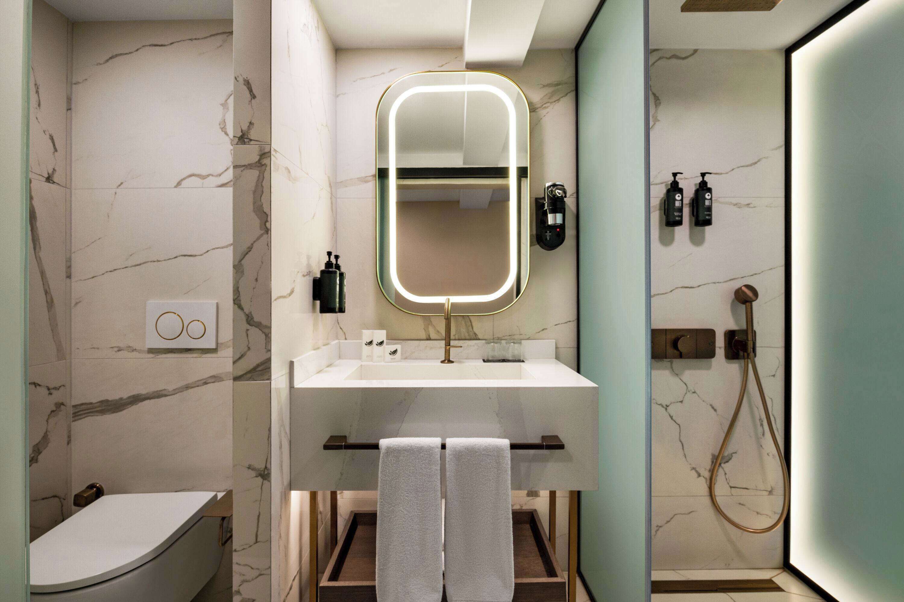 Een moderne badkamer met een marmeren wand, een grote spiegel, een wastafel en een douche.