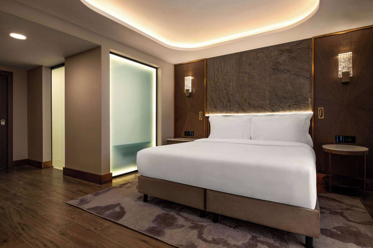 Ein modernes Hotelzimmer mit einem großen Bett, Holzboden und einer Wand mit Marmorverkleidung.